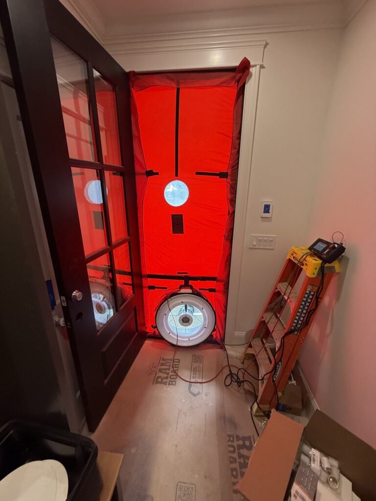 Red blower door frame and calibrated fan installed in a glass-paneled front door of a new home