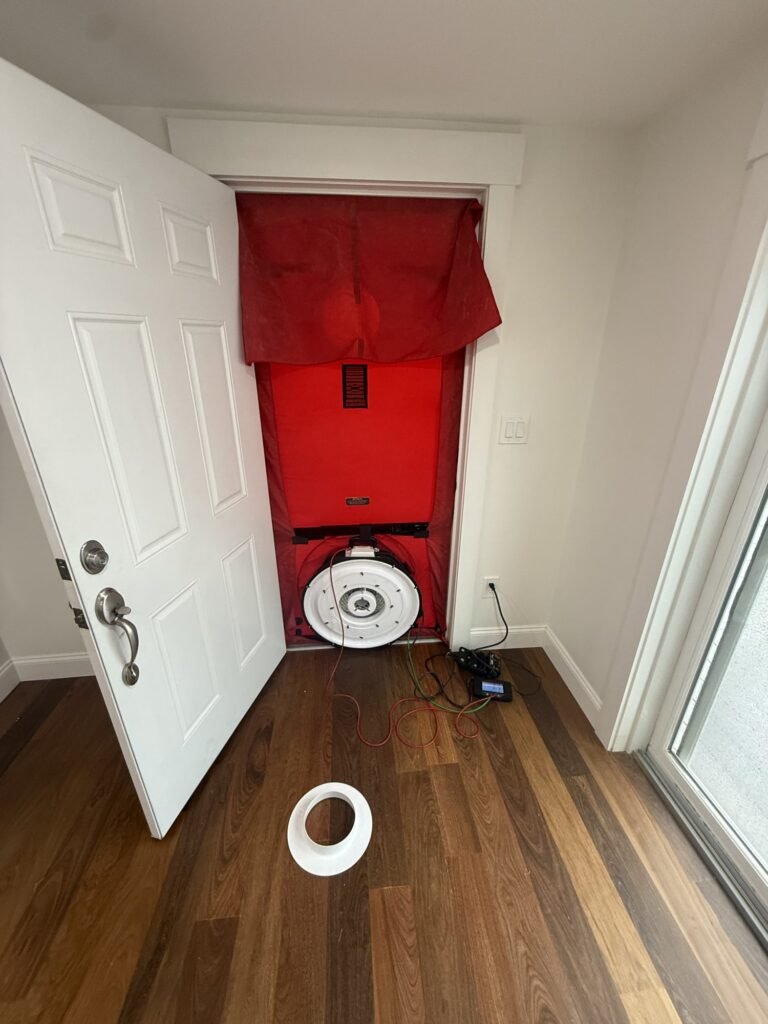 Blower door fan in a front doorway with a flow ring on the hardwood floor - blower door testing in Lynn, MA