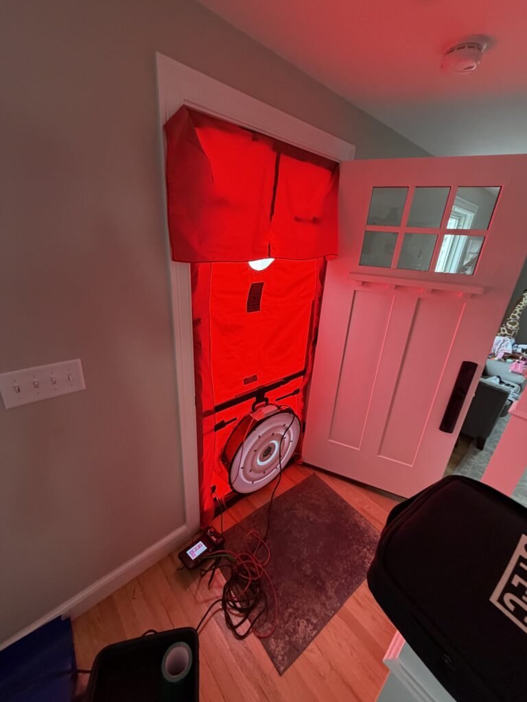 Blower door fan in a craftsman-style front door with the gauge on the floor mat – HEEC blower door testing for Ashburnham, MA homes