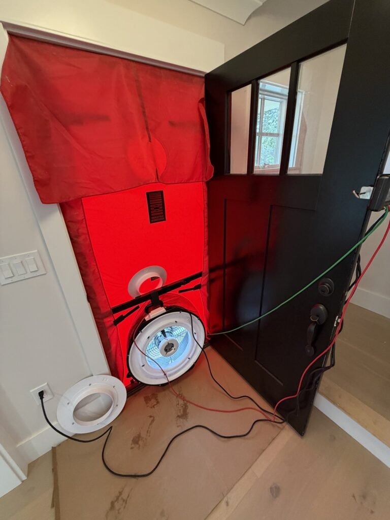 Blower door fan in a black glass-paneled front door with gauge wires attached - blower door testing in Cambridge, MA