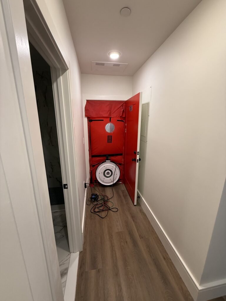 Blower door seen at the end of a long apartment hallway with recessed ceiling lights - blower door testing in Wellesley, MA