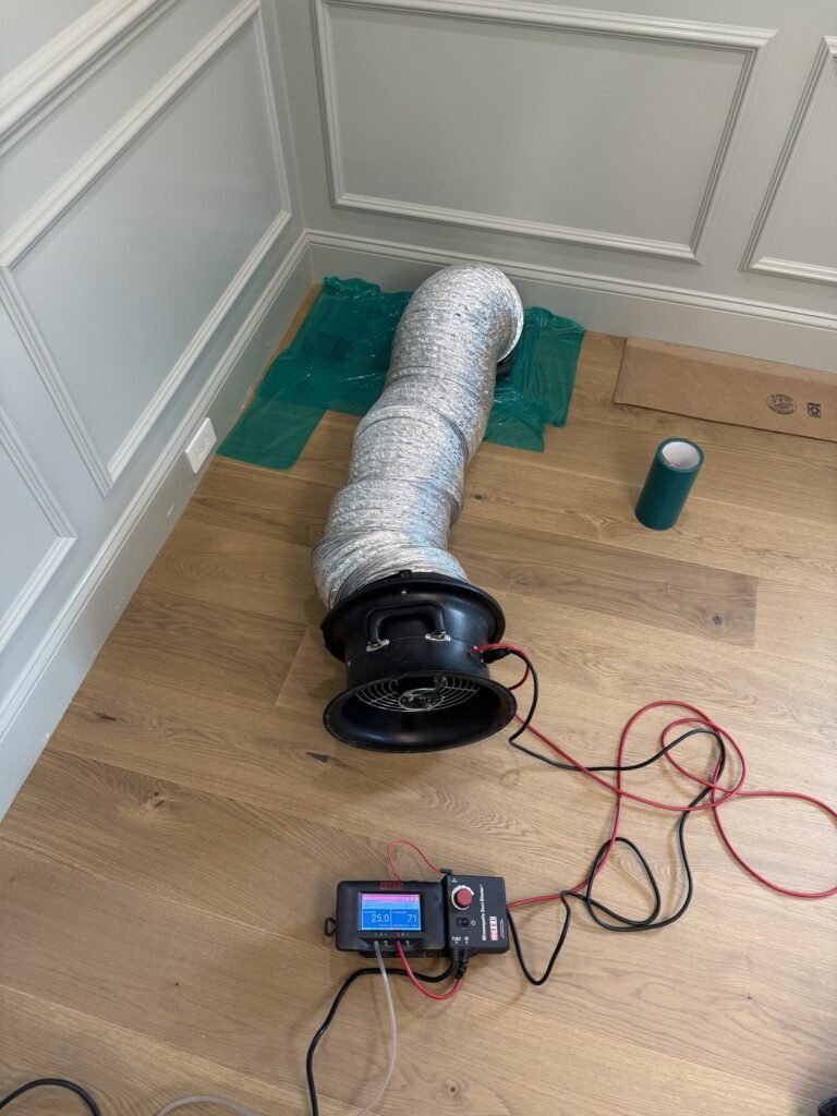 Duct Blaster fan and flex hose taped to a floor return grille in a new home with wainscoted walls – HEEC duct leakage testing for Acton, MA homes