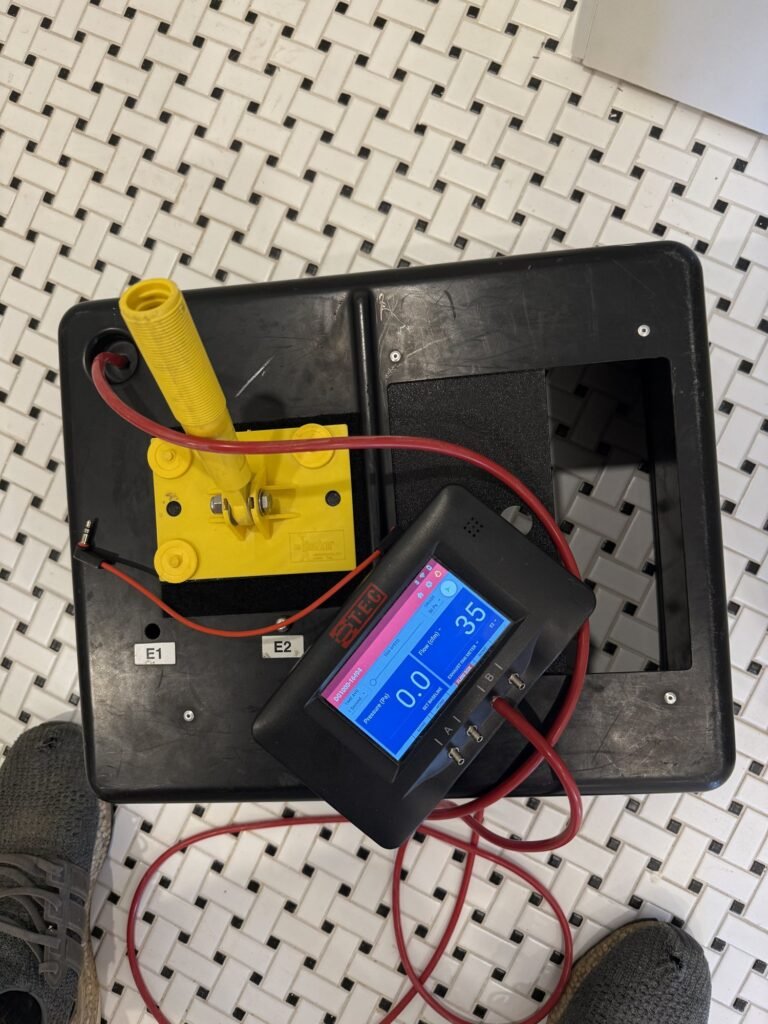 Yellow flow-ring adapter on a duct tester sitting on black-and-white tile - HERS rating in Falmouth, MA