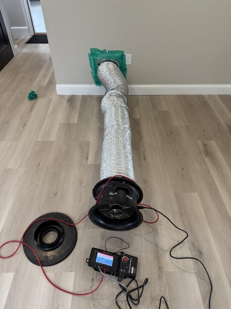 Duct Blaster hose run across a luxury vinyl plank floor to a sealed wall return grille – HEEC duct leakage testing for Montague, MA homes