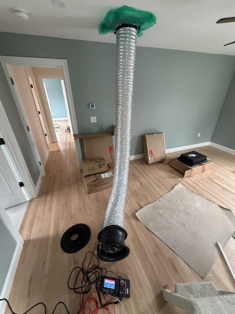 Duct Blaster hose running up to a ceiling return grille in a new home with gray walls – HEEC duct leakage testing for Reading, MA homes