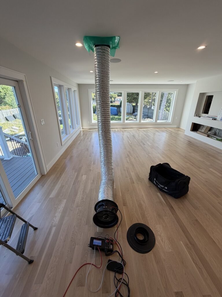 Duct Blaster hose rising to a ceiling return grille in a large open new-construction great room – HEEC duct leakage testing for Brookfield, MA homes