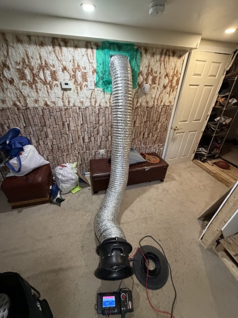 Duct Blaster hose taped to a high wall return grille in a bedroom with a stone accent wall – HEEC duct leakage testing for Springfield, MA homes