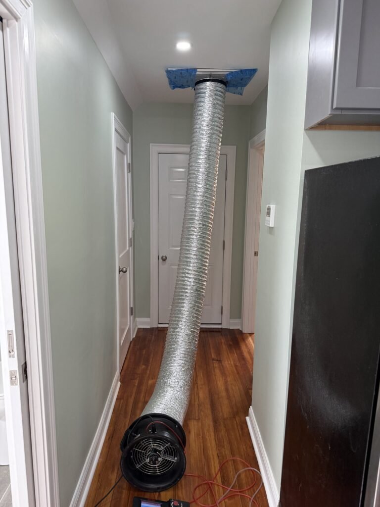 Duct Blaster hose run down a hallway to a ceiling return grille sealed with blue tape – HEEC duct leakage testing for Sterling, MA homes