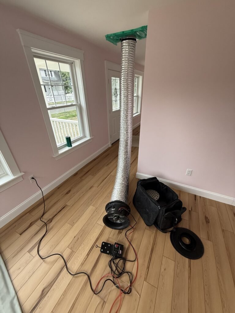 Duct Blaster hose rising to a ceiling return grille in a new home with a pink-painted room – HEEC duct leakage testing for Freetown, MA homes