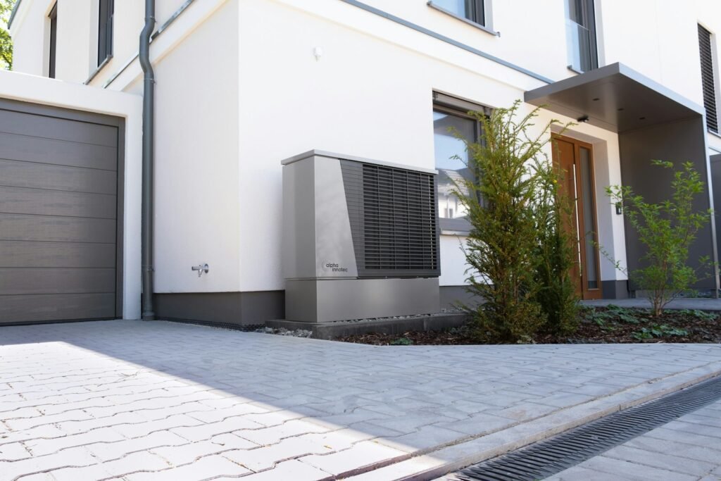 White modern home with a heat pump unit beside the paved driveway - HERS rating in Chelmsford, MA