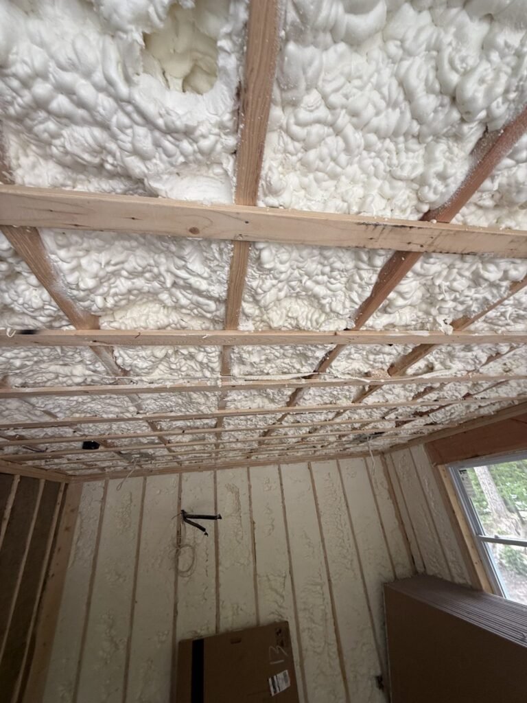 Thick spray-foamed ceiling bays above wood strapping in a room with a window - HERS rating in Marshfield, MA