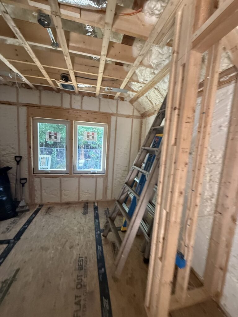 Long room with two windows, foamed walls and a ladder under open ceiling framing - spray foam insulation in Ludlow, MA