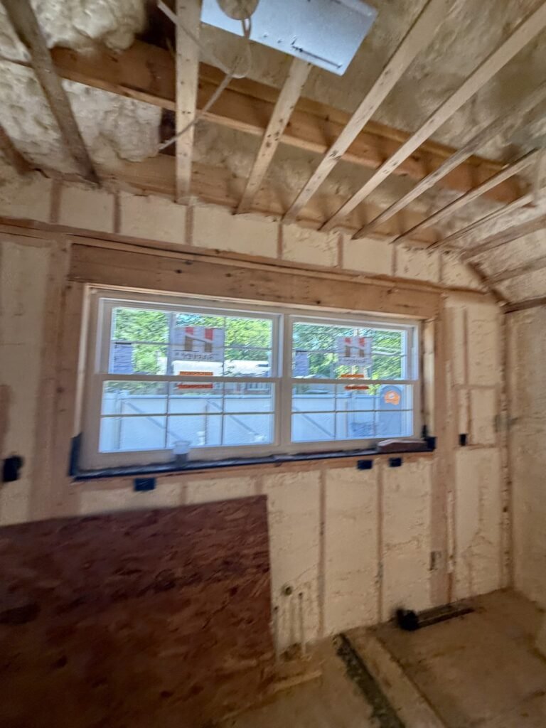 Foamed walls and sloped ceiling around a wide double window with plywood below - spray foam insulation in Townsend, MA